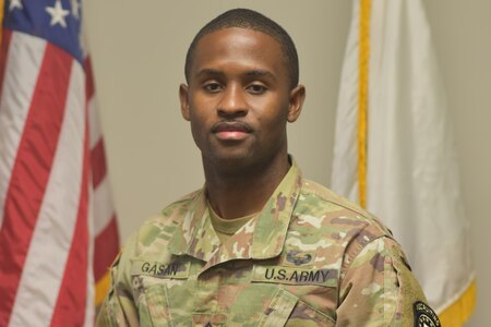 Soldier in uniform standing in front of flag.