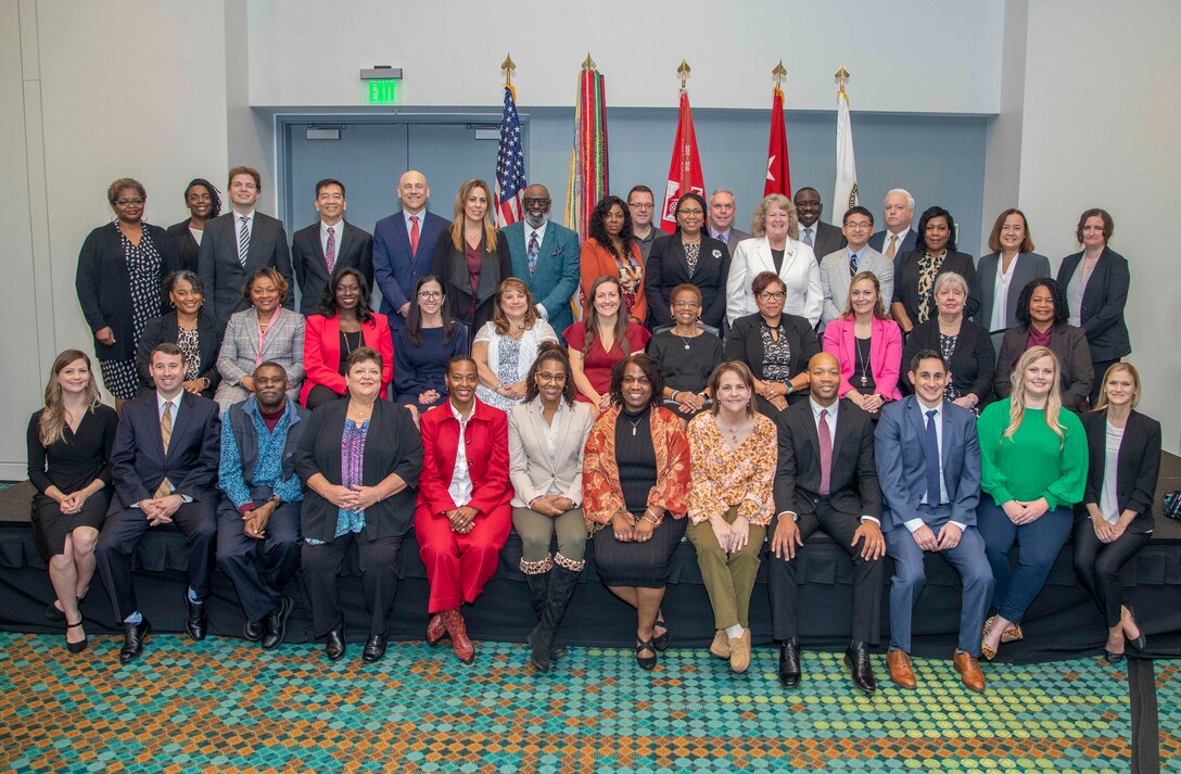 Photo of a group of people posing for a photo in front of the US flag, US Corps of Engineers flag.