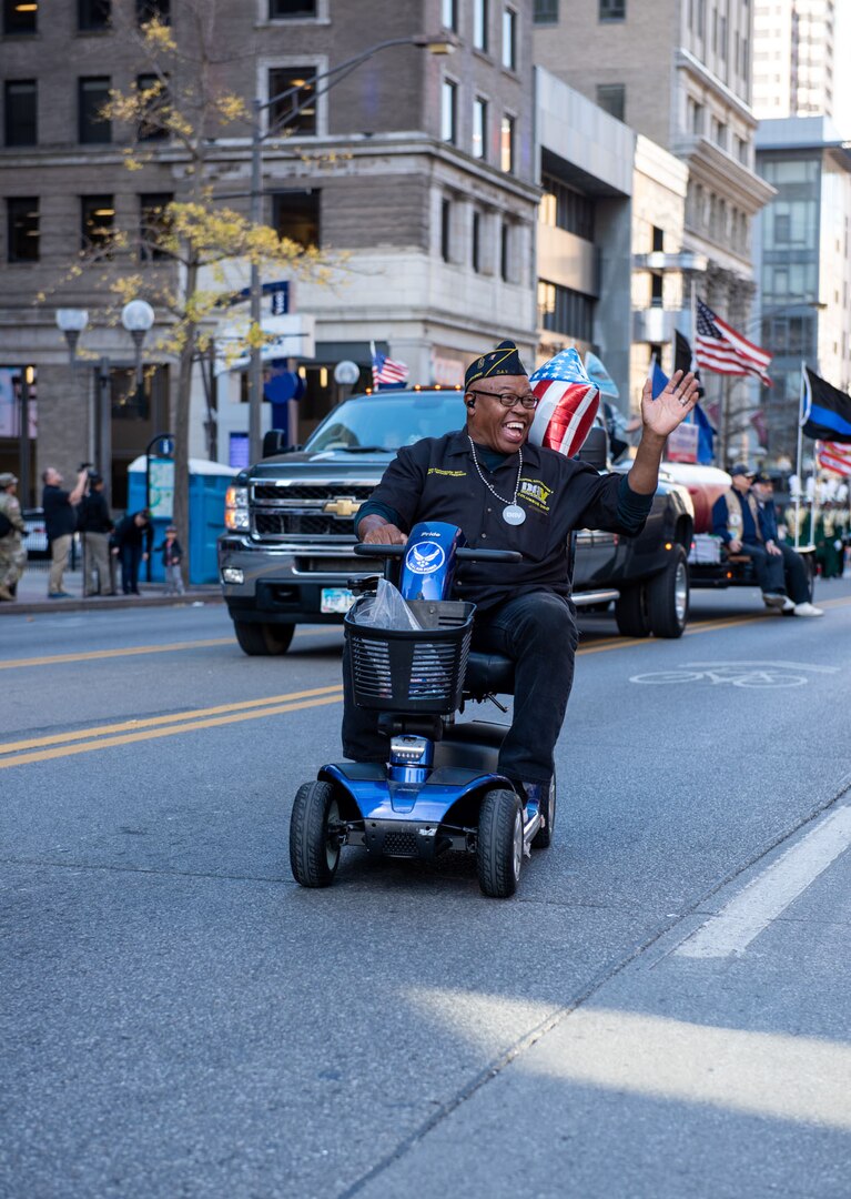 A man with a American Legion hat on hat rides in the parade on his scooter.