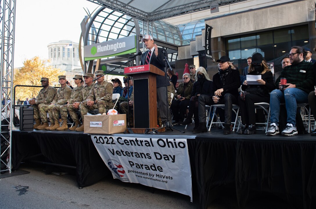 A viewing stand of military members and civilians with a speaker at the podium.