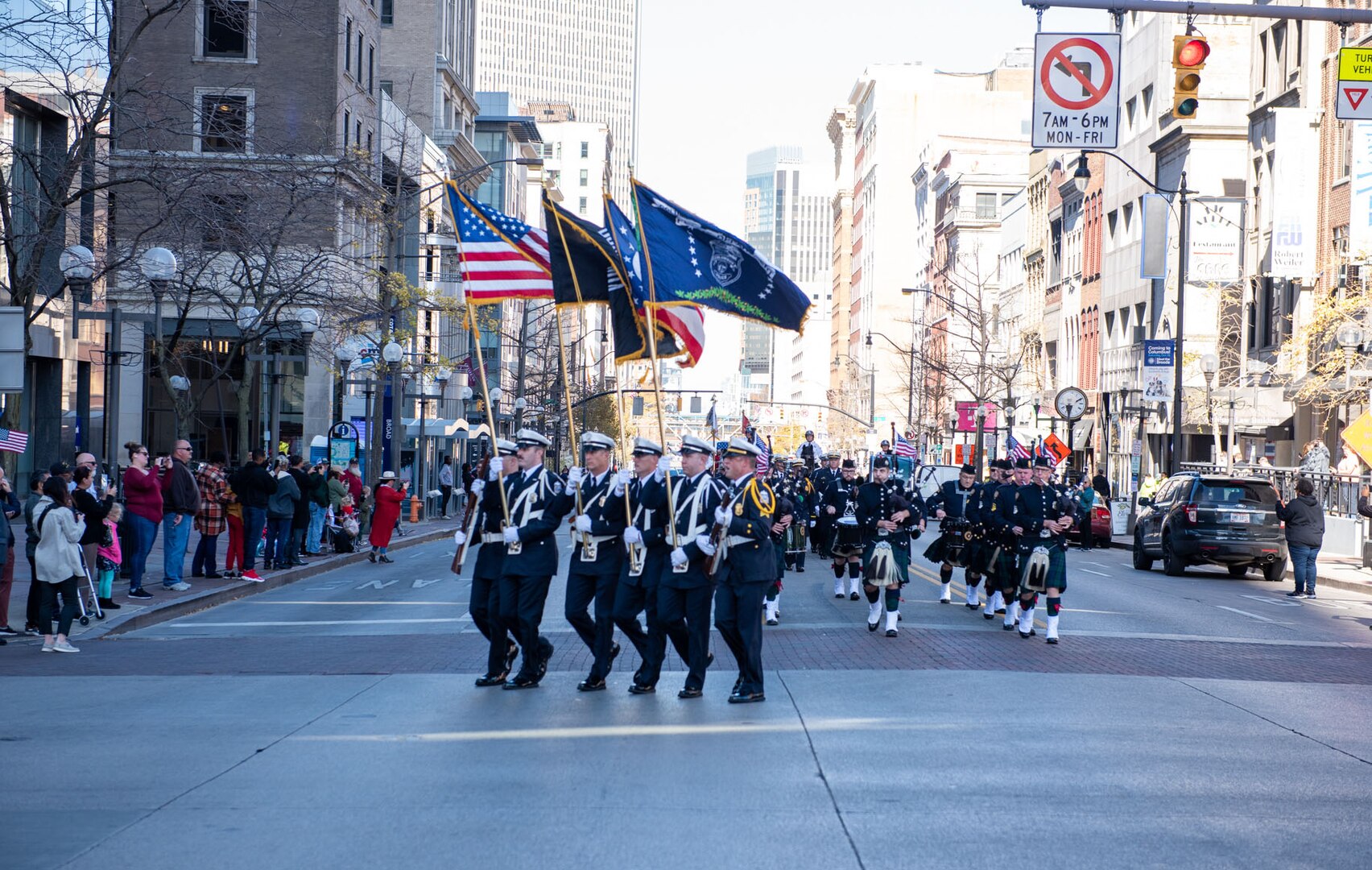 A police unit comprised of more than 50 members march down a street in between high-rise buildings.