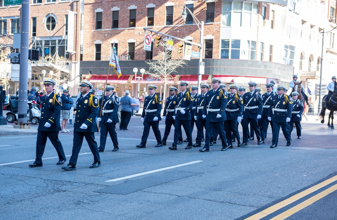 A police unit consisting of about 40 members march down a street in between high-rise buildings.