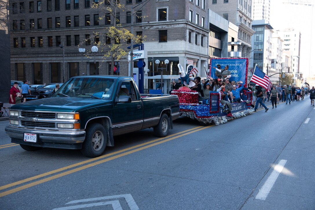 A green pickup truck pulls a trailer decorated to be a patriotic float with several people on it waving.