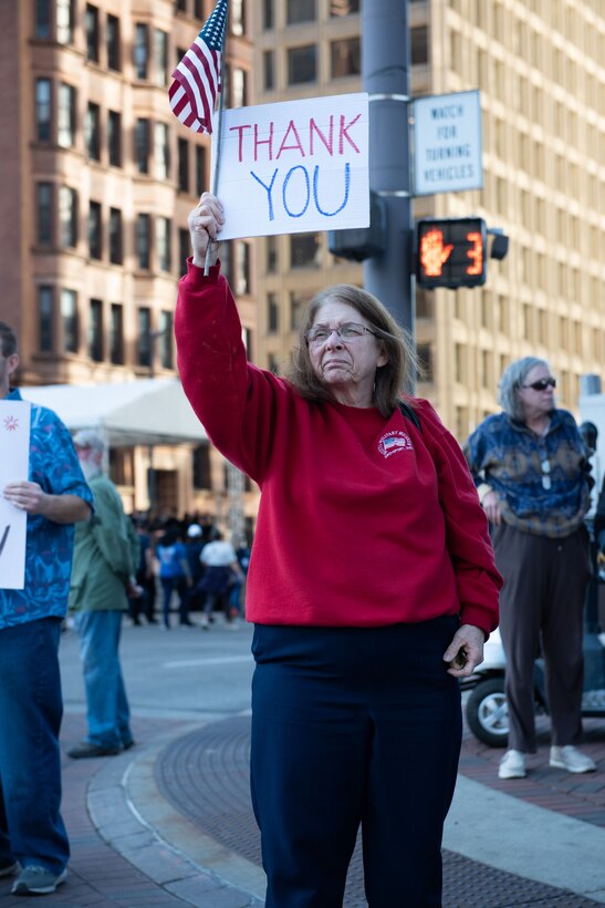 A dark haired woman holds a sign while standing on the street.