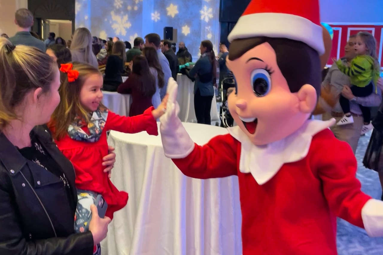 A little girl high-fives a life-sized elf.