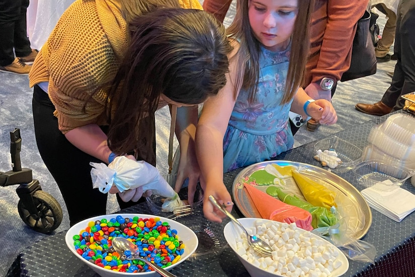 A woman and a girl decorate cookies with toppings and icing.