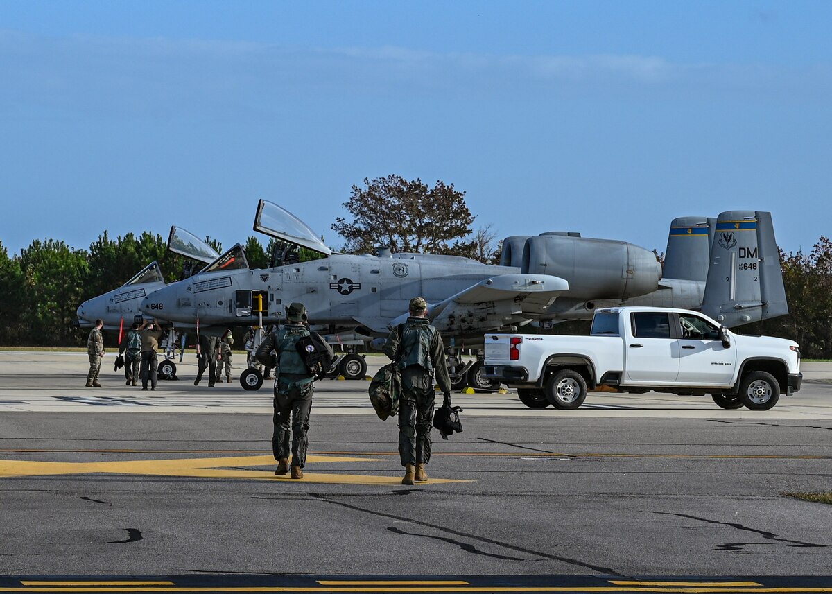 A photo of pilots in military uniforms walking towards military aircraft.