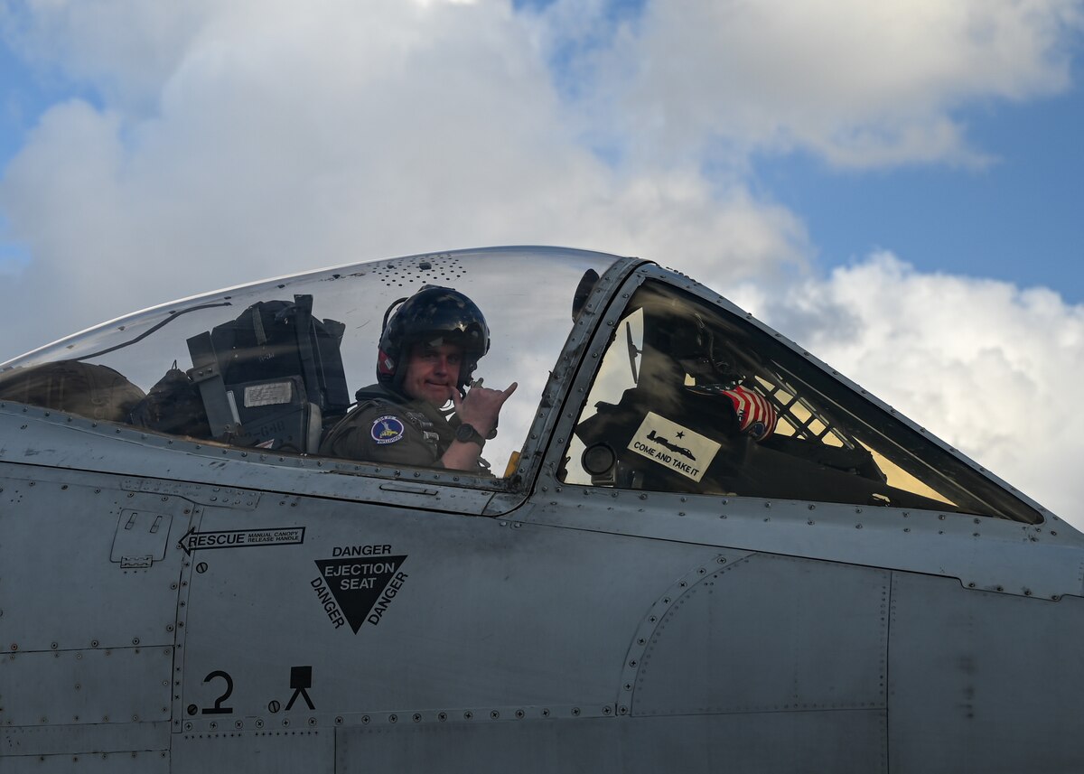 A photo of a pilot in a military uniform in the cockpit of a military aircraft.