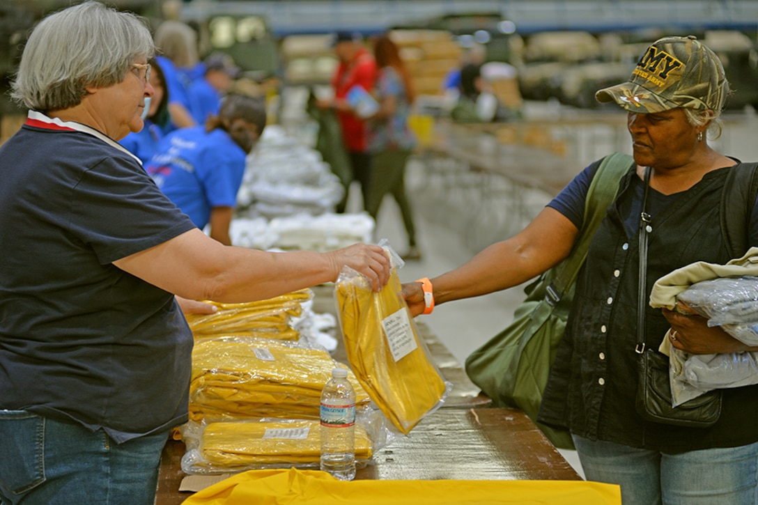 A woman hands another woman a poncho.