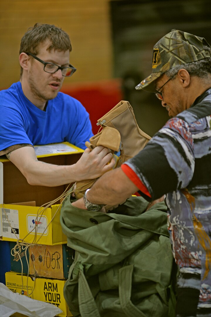 A man helps put a pair of boots into another man's bag.