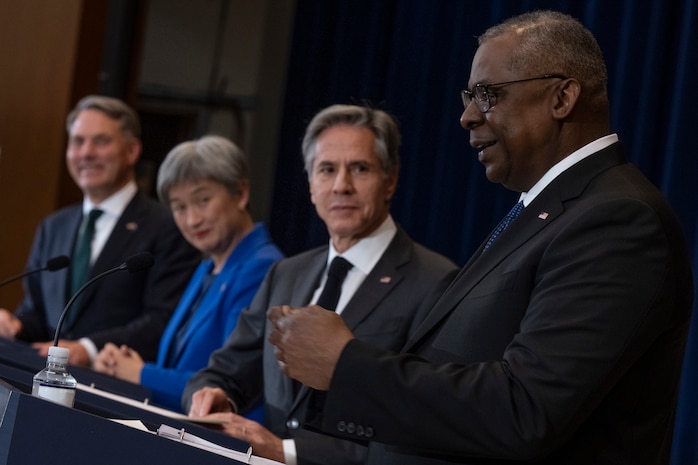 Three men and one woman stand abreast of one another behind lecterns.