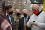 A group of four men wearing face masks stand looking at a phone screen.