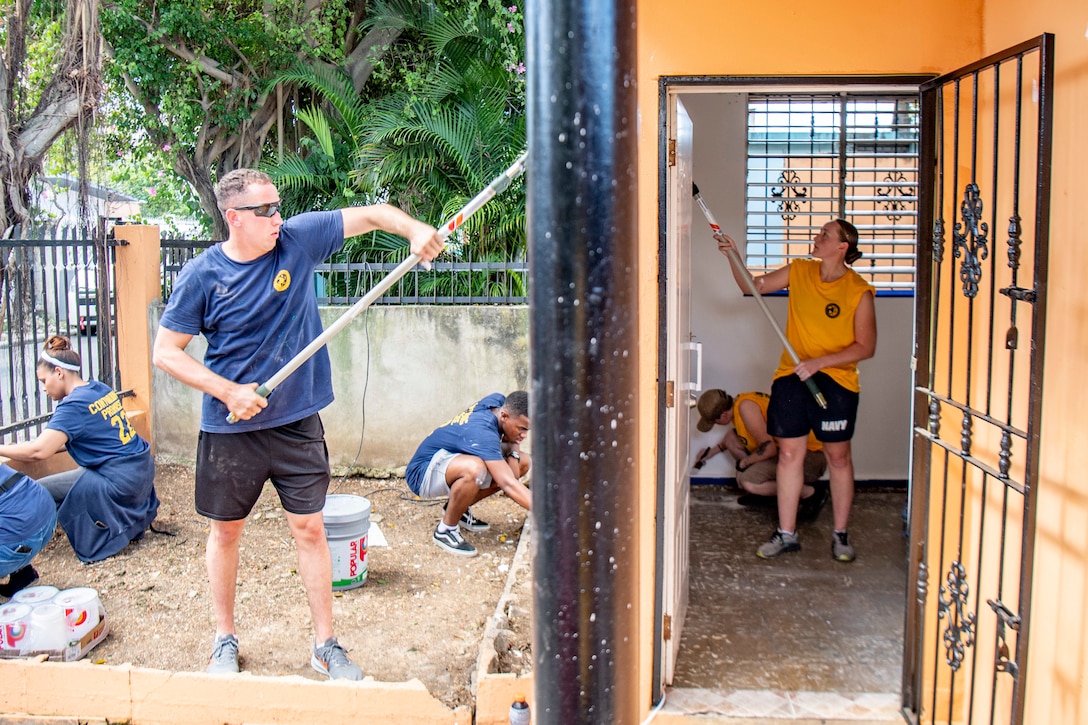 Service members paint walls and do other work around a building.