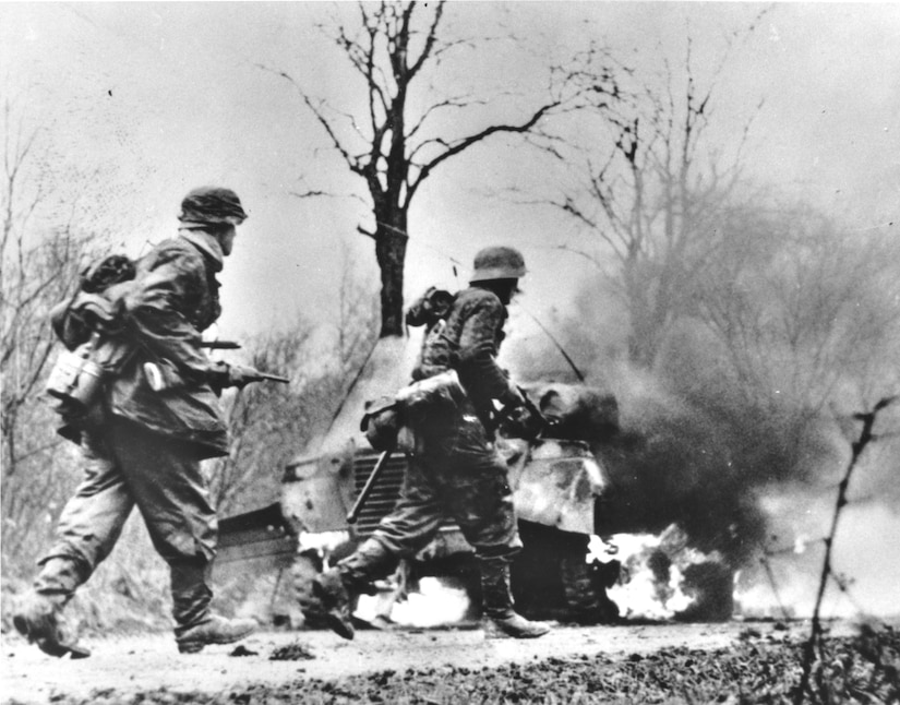 Two men walk past a burning vehicle.