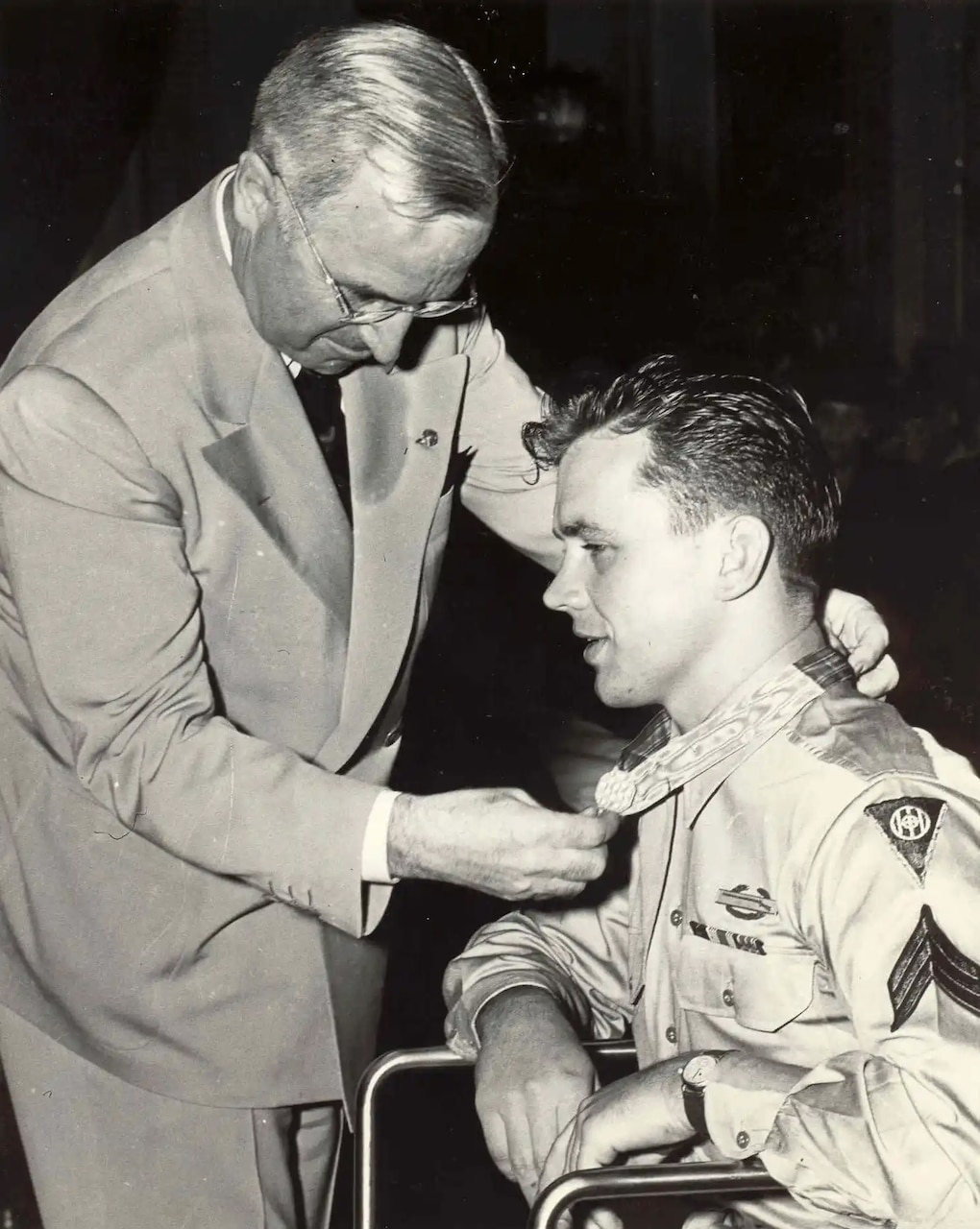 A man puts a medal around the neck of seated man.