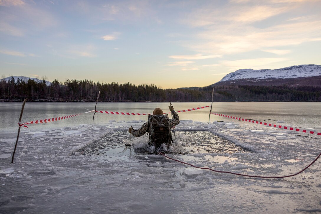 A Marine jumps into a square water hole carved in a field of ice.