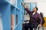 Person in wheelchair reaching for book in library.