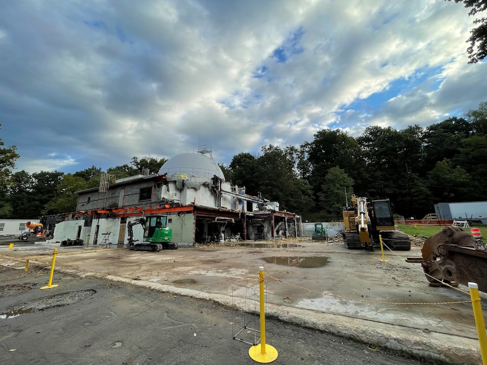 Demolition building in front of trees and construction site.