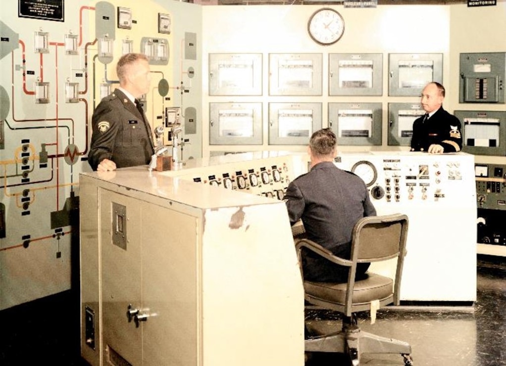 Three men discuss amongst each other in the SM-1 control room.
