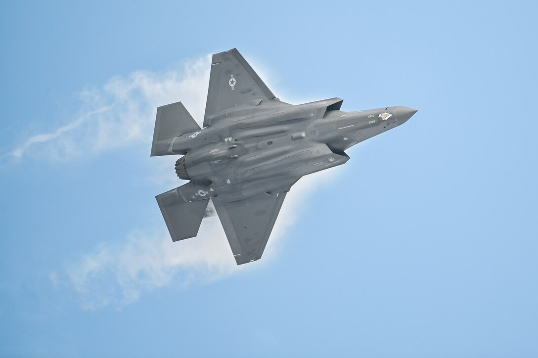 An Air Force jet creates vapor trails while flying in blue sky.