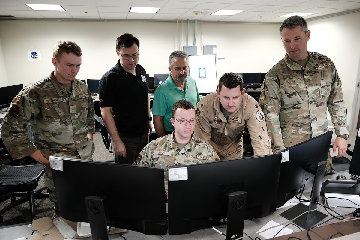 four military members and two civilians work in an office environment on computers.