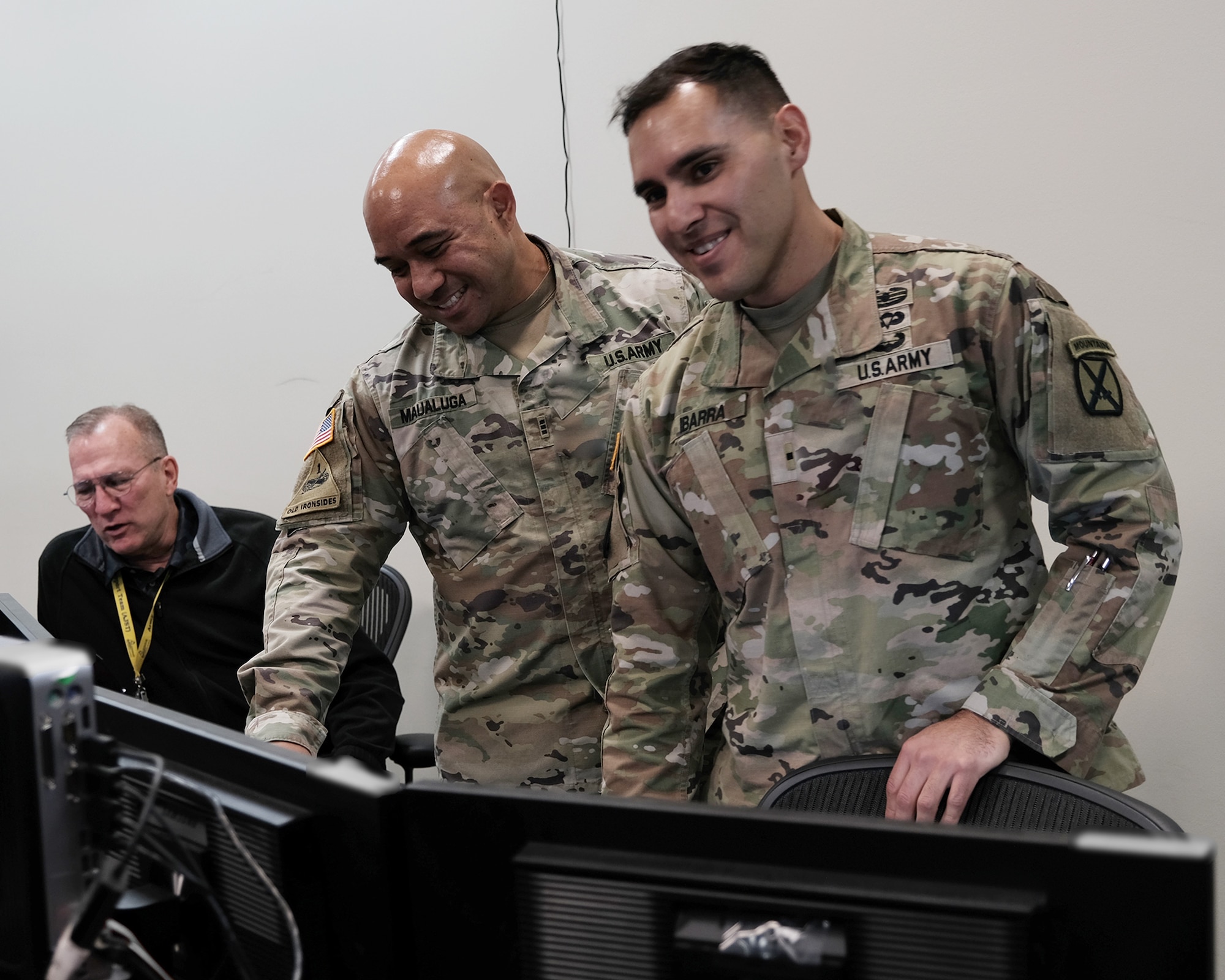 two military members nd a civilian work in an office environment on computers.