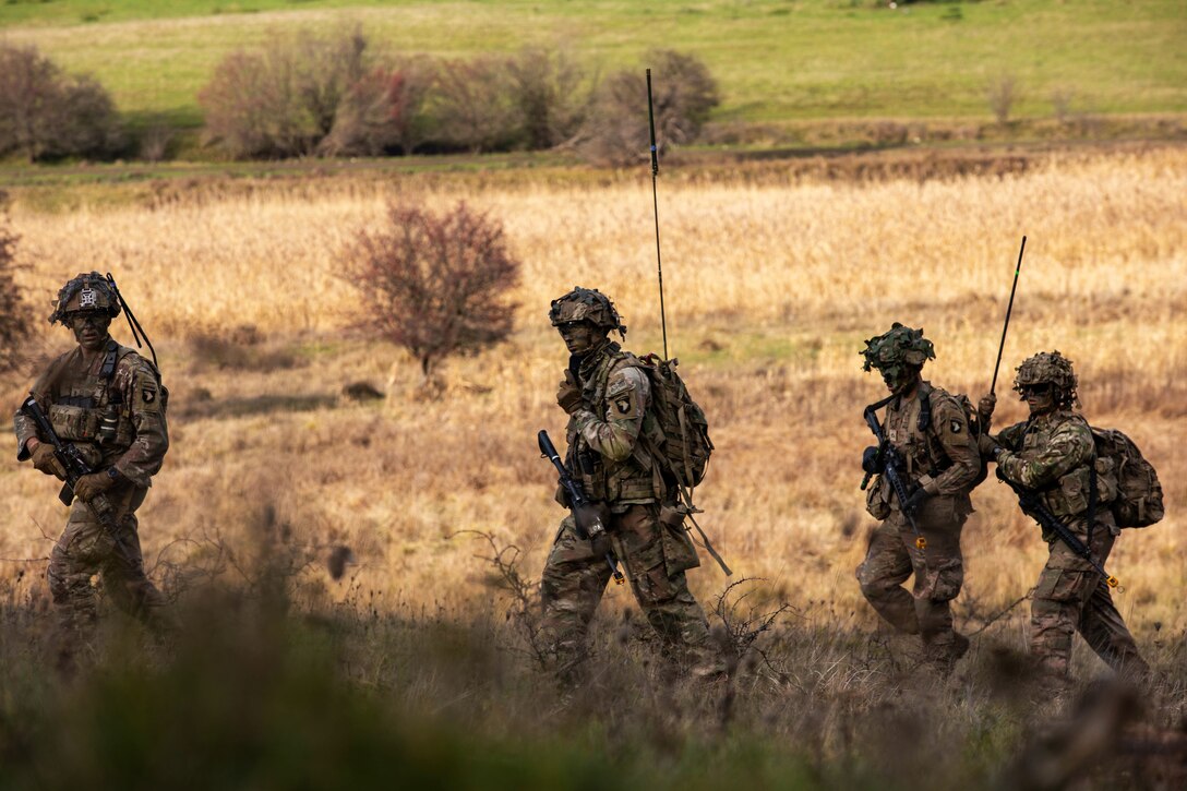 Soldiers carrying weapons walk through a field.