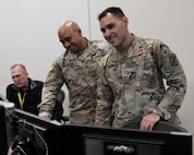 two military members nd a civilian work in an office environment on computers.