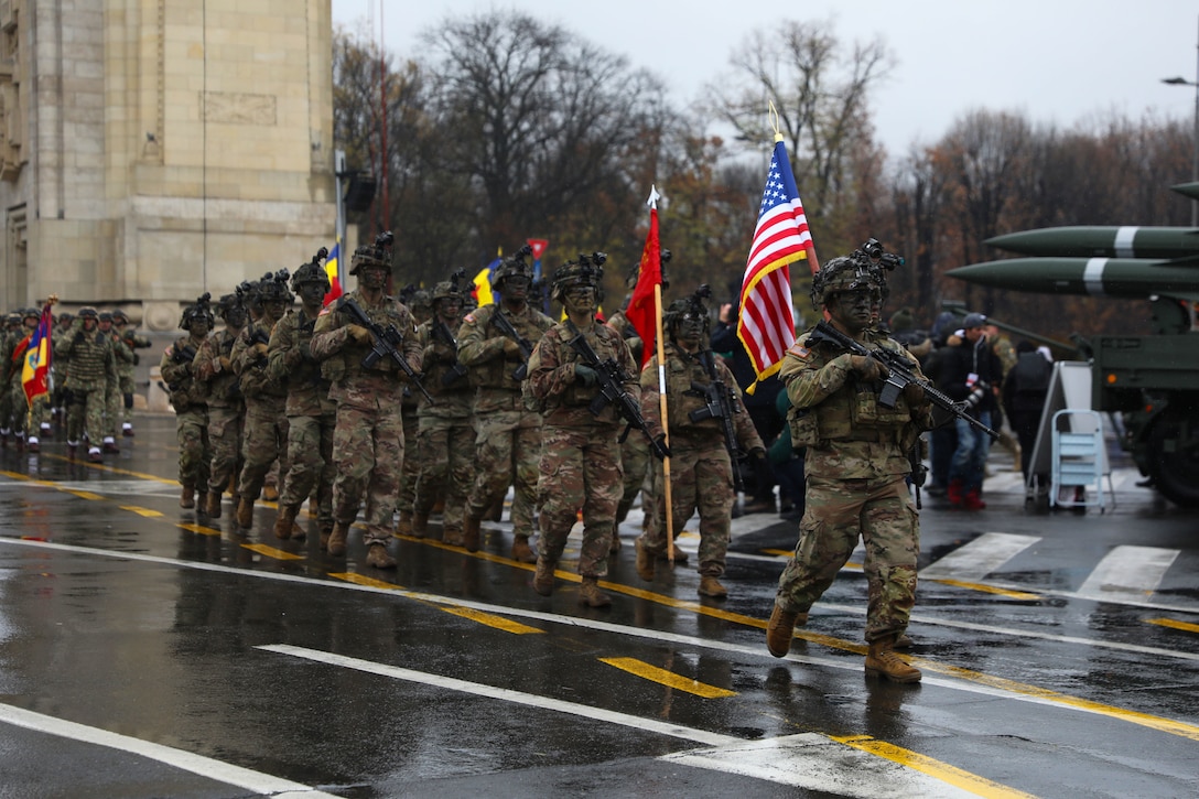 Soldiers carrying weapons and flags march in a parade.