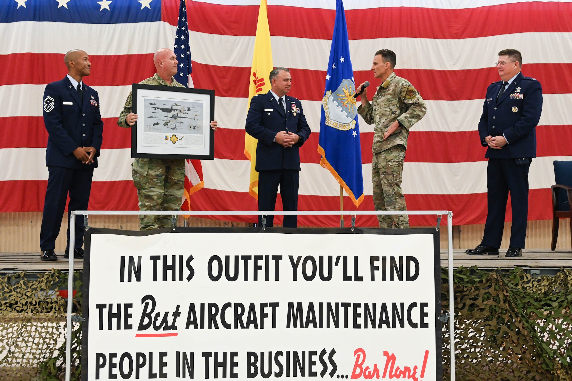 Uniformed Air Force members on stage giving a gift to a retiring lieutenant colonel.