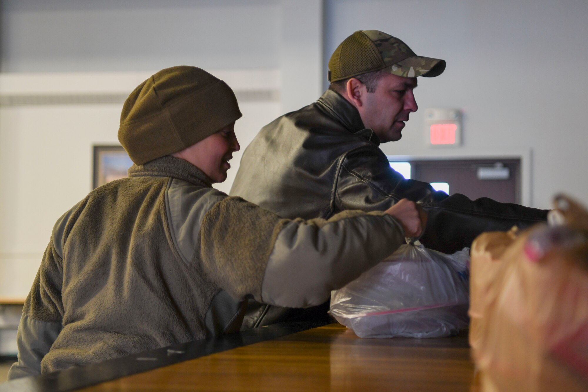 A man and a women in green uniforms take bags of cookies off of a table.