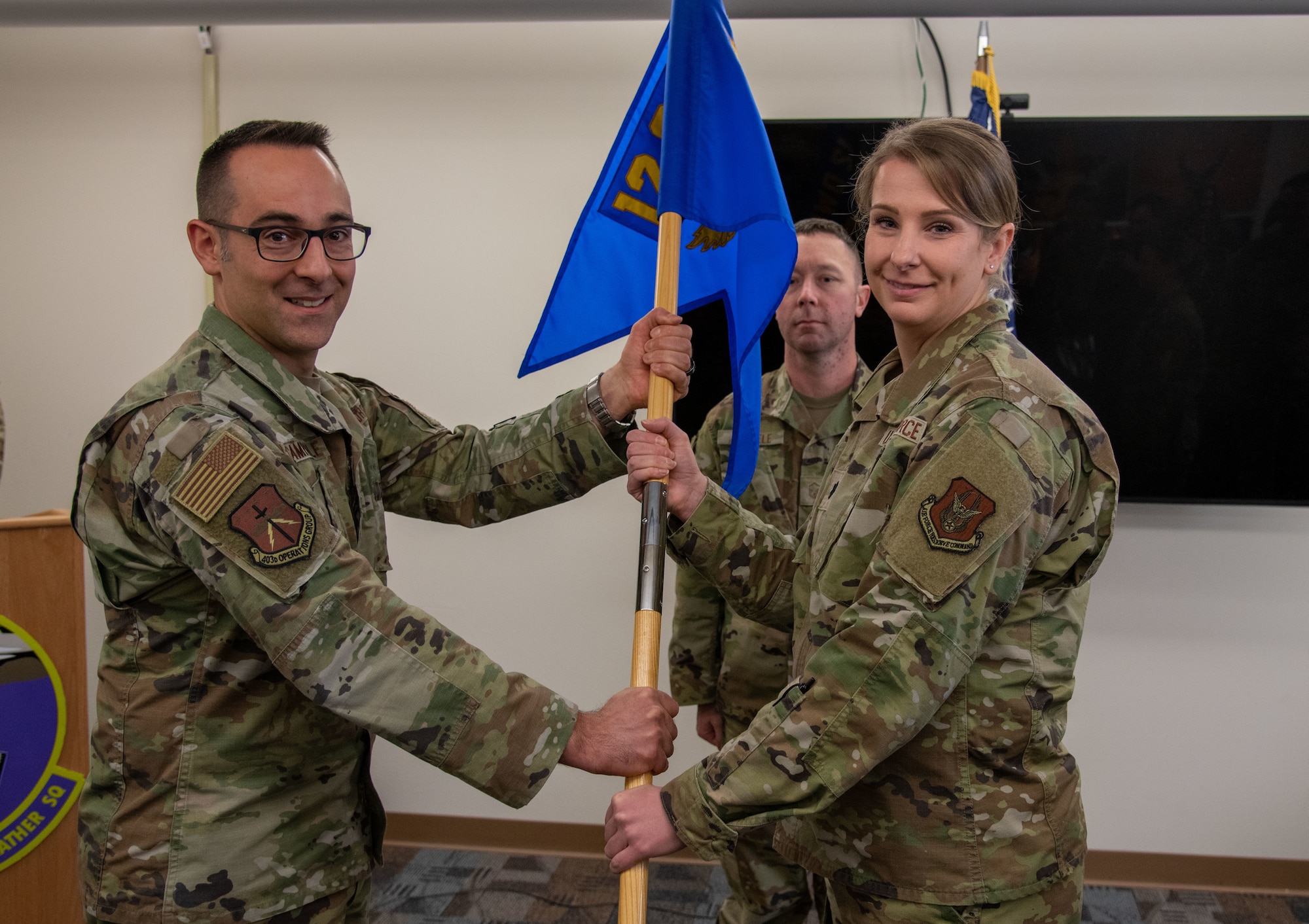 Col. Campanile and Lt. Col. Fennwald both hold the guidon as another Airman stands behind them