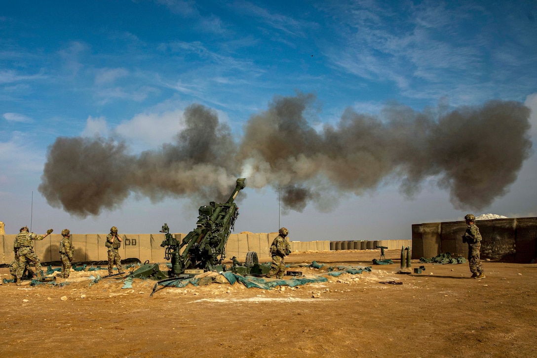 A cloud of smoke forms above soldiers in a desert-like area after firing a weapon.