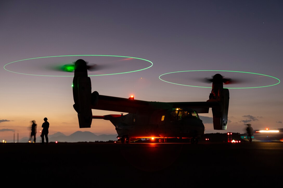 An Osprey aircraft sits on the tarmac at night.