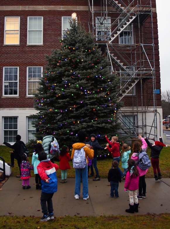 Children stand around a lighting Christmas tree.