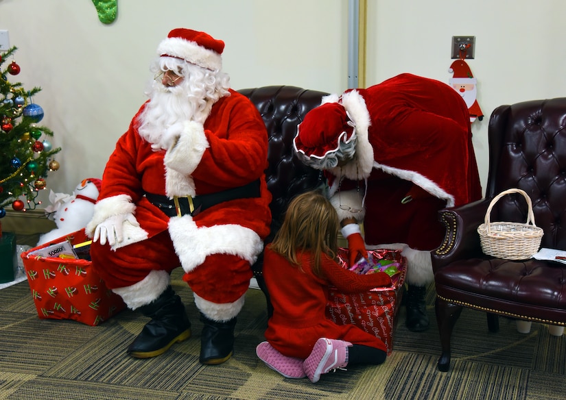 Mr. and Mrs. Claus give a present to a child.