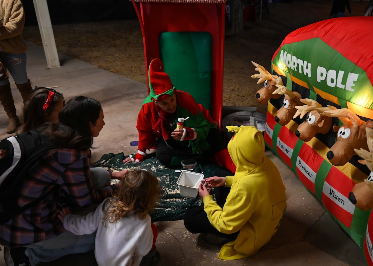 A photo of a woman dressed as an elf doing arts and crafts with a group of children.