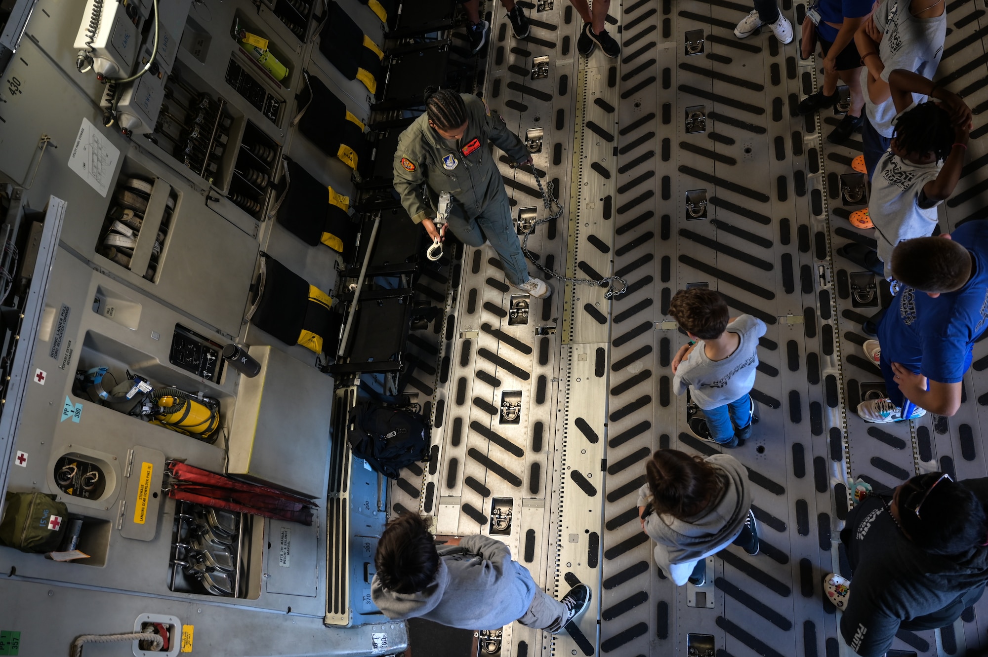 Airman 1st Class Taylor Williams, 535th Airlift Squadron C-17 Globemaster III loadmaster, demonstrates cargo securing techniques to students from Aliamanu Middle School during a base tour at Joint Base Pearl Harbor-Hickam, Hawaii, Nov. 22, 2022. Williams shared the importance of her job inside the aircraft as an aircrew member serving in the Indo-Pacific theater. (U.S. Air Force photo by Staff Sgt. Alan Ricker)