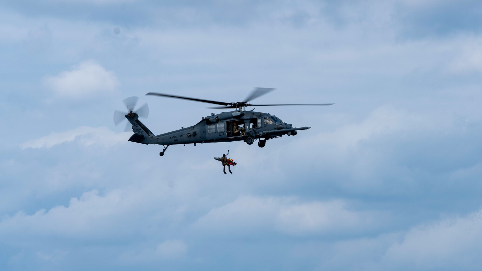 A helicopter flies with a person hanging from it.