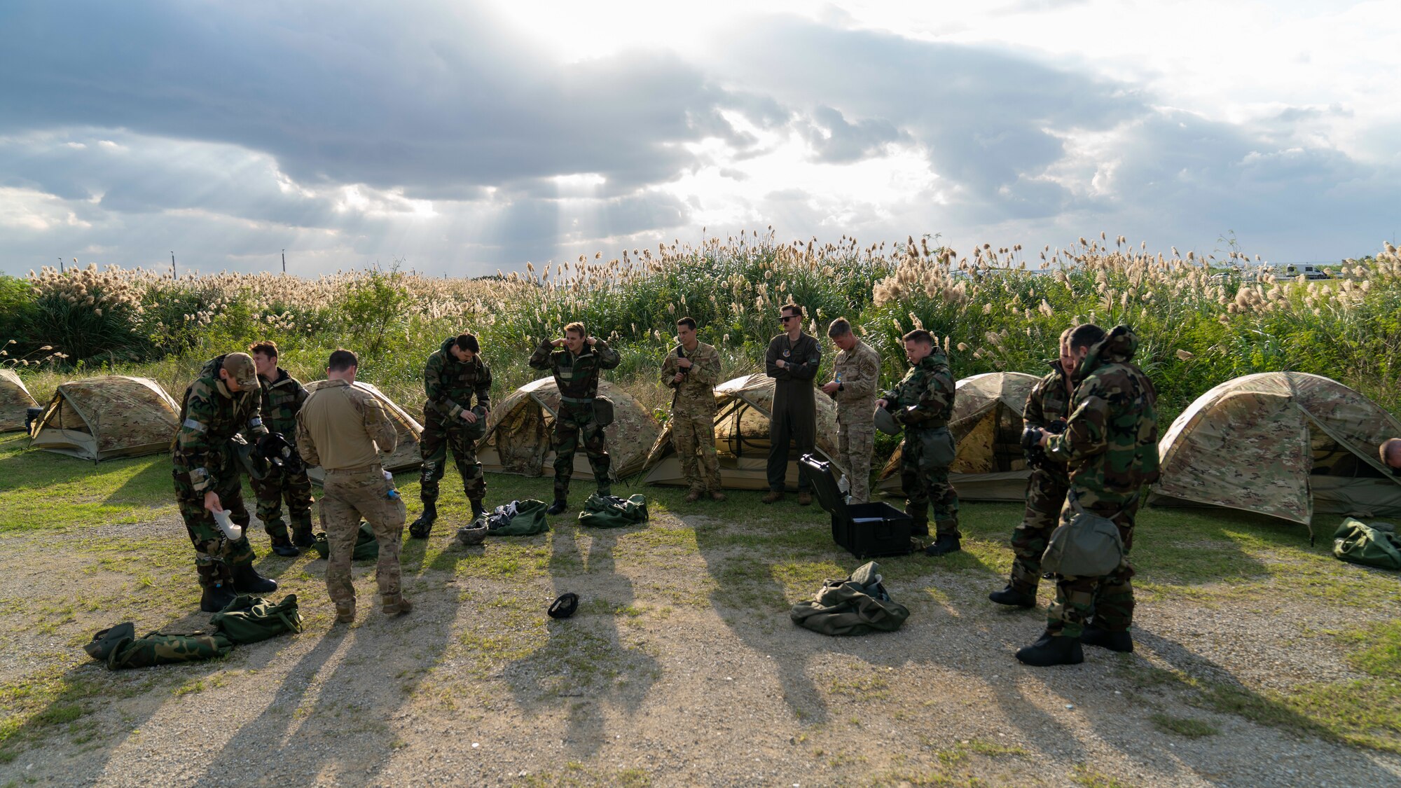 Airmen put on mission oriented protective posture gear in a field on a sunny day.