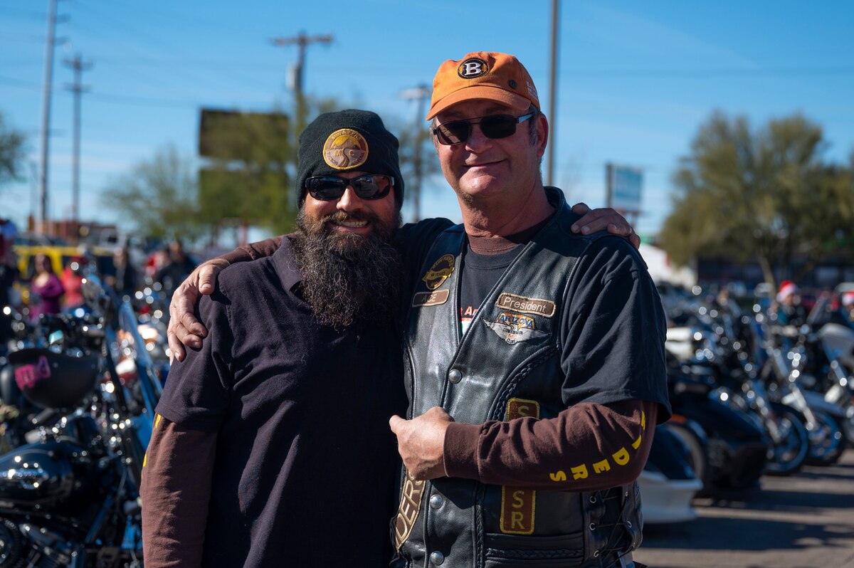 A photo of two men smiling in front of parked motorcycles.