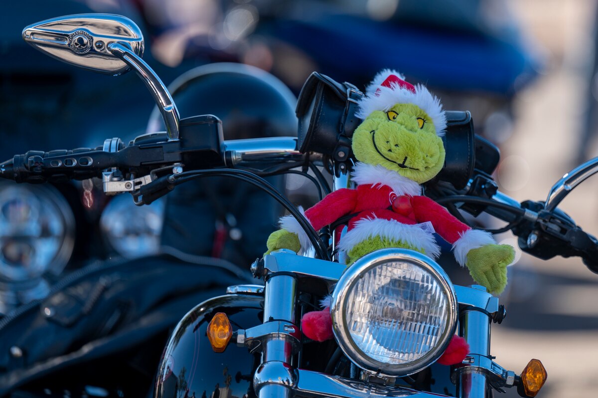 A photo of a green stuffed toy dressed in a Santa suit placed on a motorcycle.