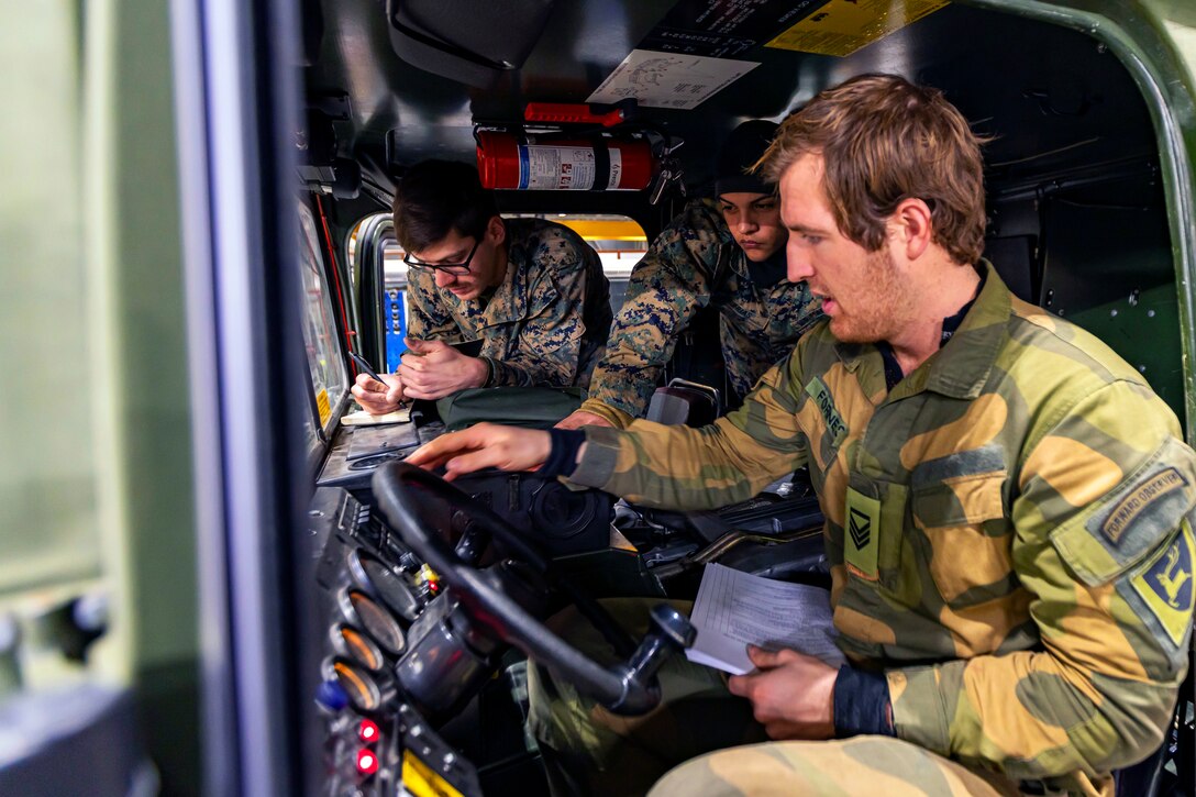 A foreign service member speaks to Marines while behind a vehicle's wheel.