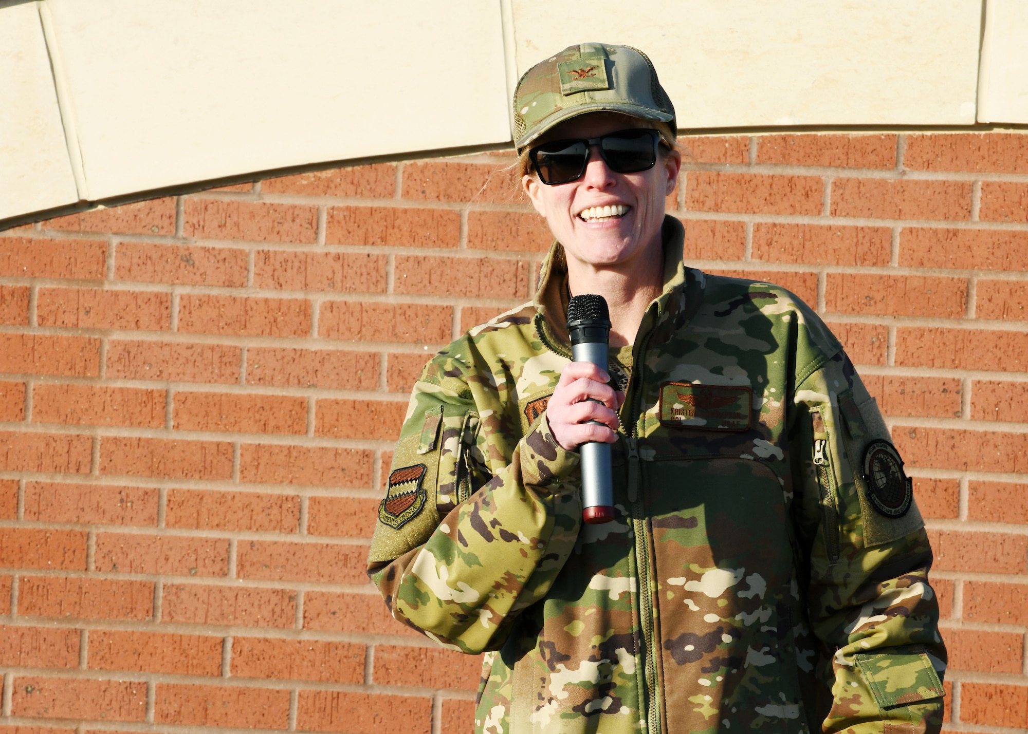 Military member stands in front of brick wall and addresses a crowd of sheriff department members.