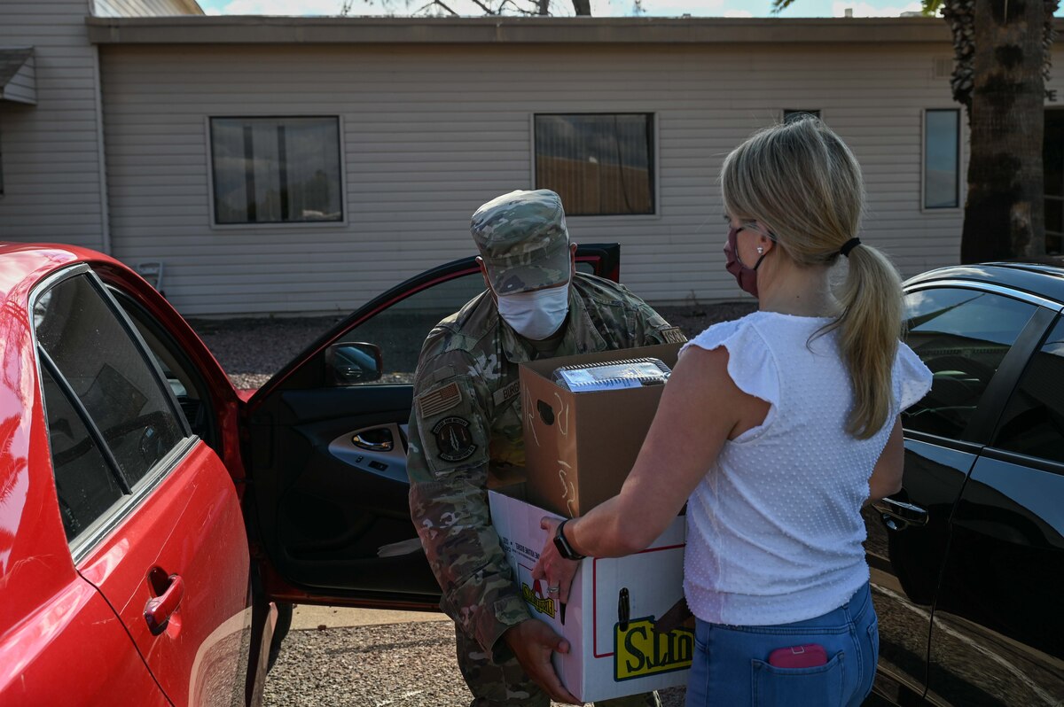 A photo of a woman handing boxes of cookies to a man in a military uniform.