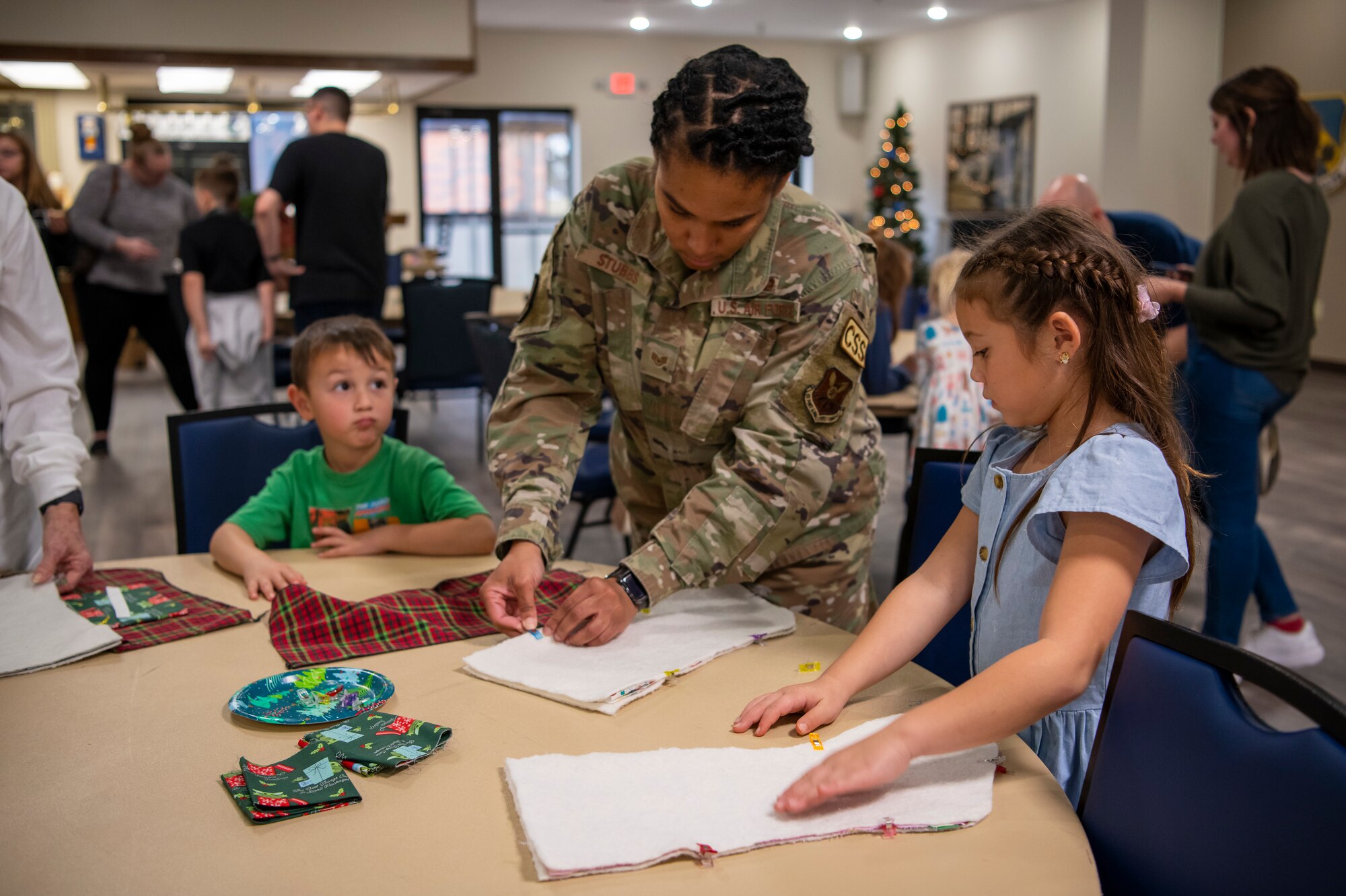 A volunteer shows a military child how to pin their stocking fabric.