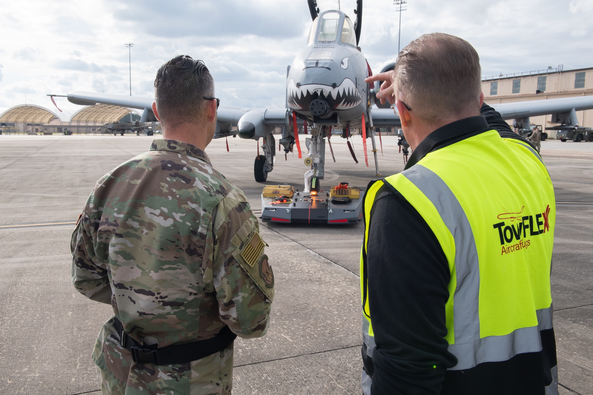 Two people on the flightline watching a plane get towed.