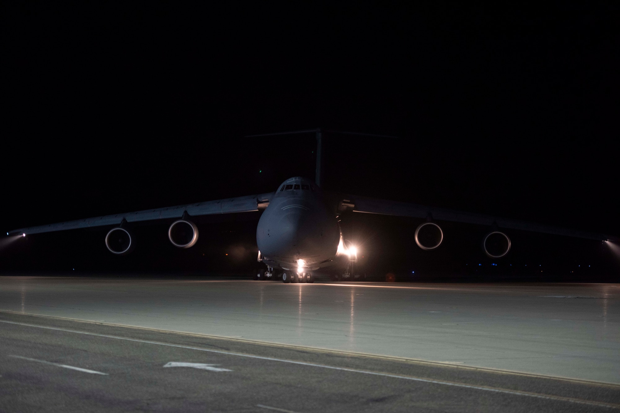 A large military aircraft drives on the flight line at night.