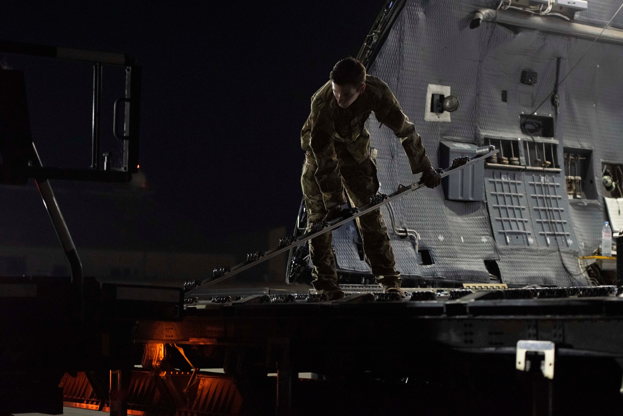 An Airman puts down a roller from a large aircraft onto a vehicle.