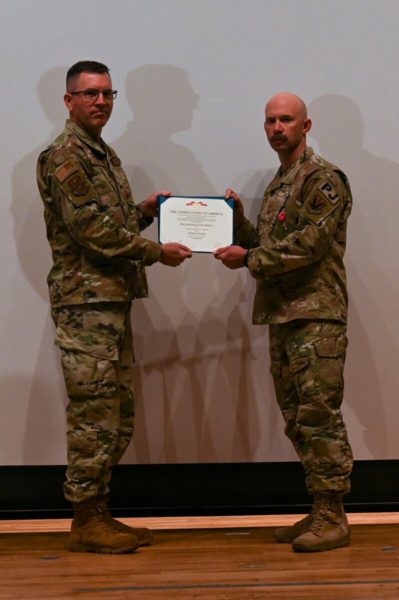 A photo of a man in a military uniform receives a certificate from another man in uniform.